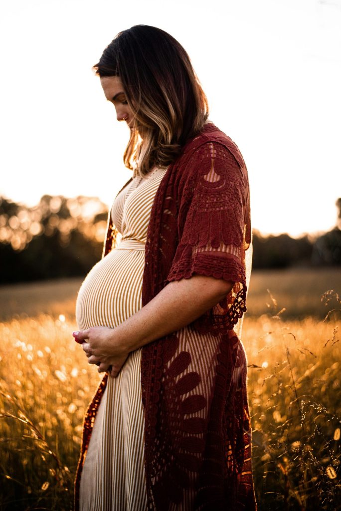 Photo de femme enceinte devant un champ de blé, avec un soleil couchant